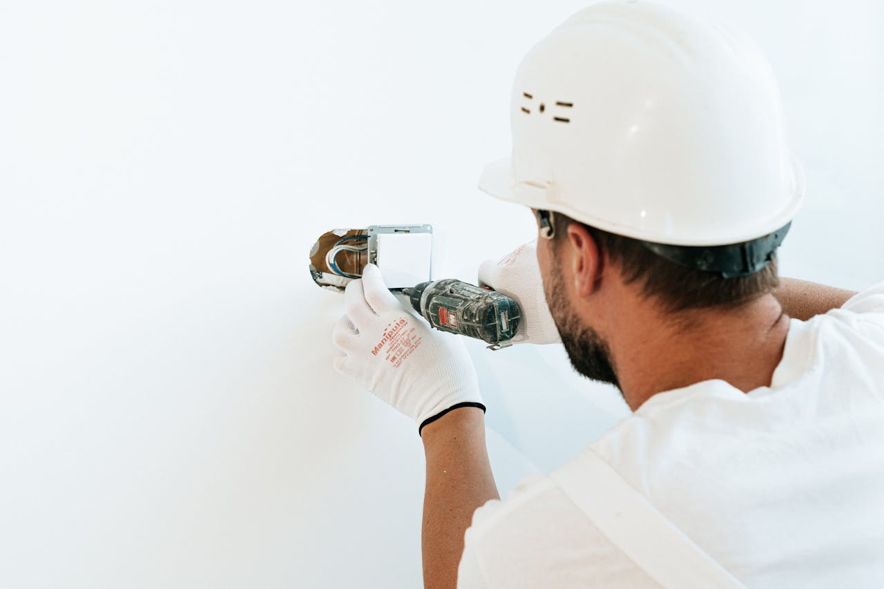 Construction worker wearing helmet and gloves uses a power tool to fix a wall.