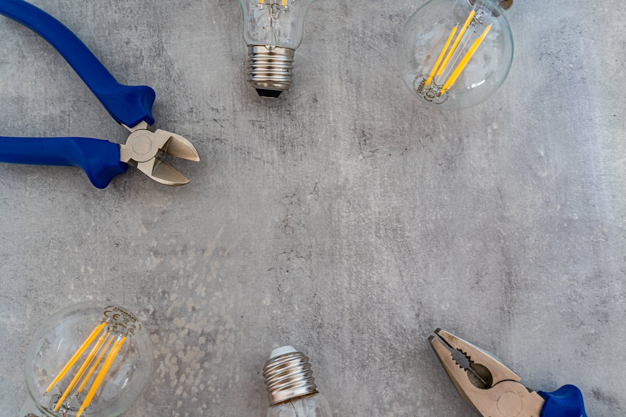 A flat lay image featuring clear light bulbs and pliers on a gray surface, ideal for technology themes.